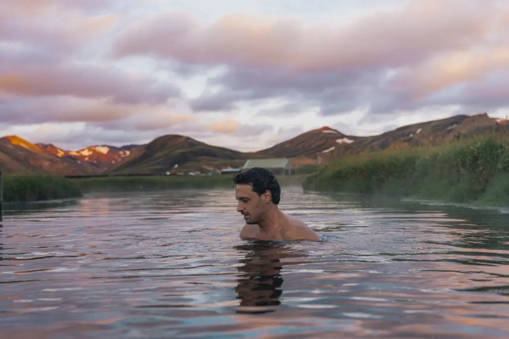 homme se baignant dans une source chaude avec les montagnes au coucher du soleil