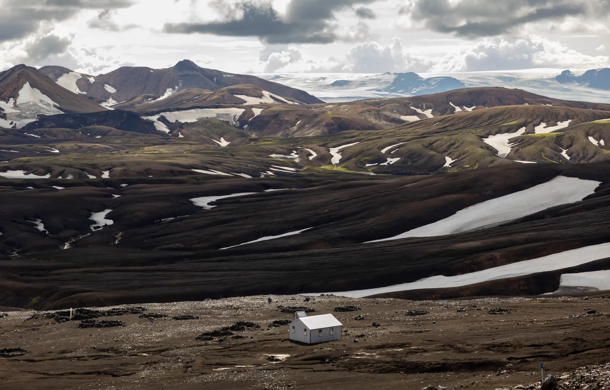 petite cabane blanche dans un vaste paysage volcanique parsemé de plaques de neige